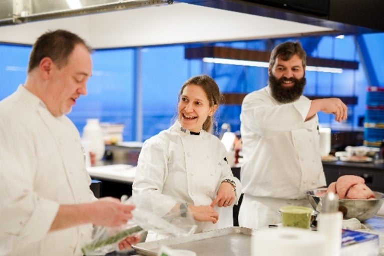 Three chefs in white uniforms preparing food in a modern kitchen.