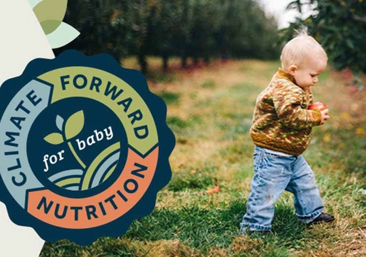 Toddler holding an apple in an orchard with a “Climate Forward Nutrition” badge