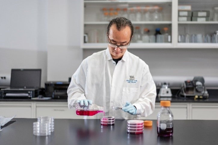 Scientist in a lab coat working with petri dishes on a laboratory bench.