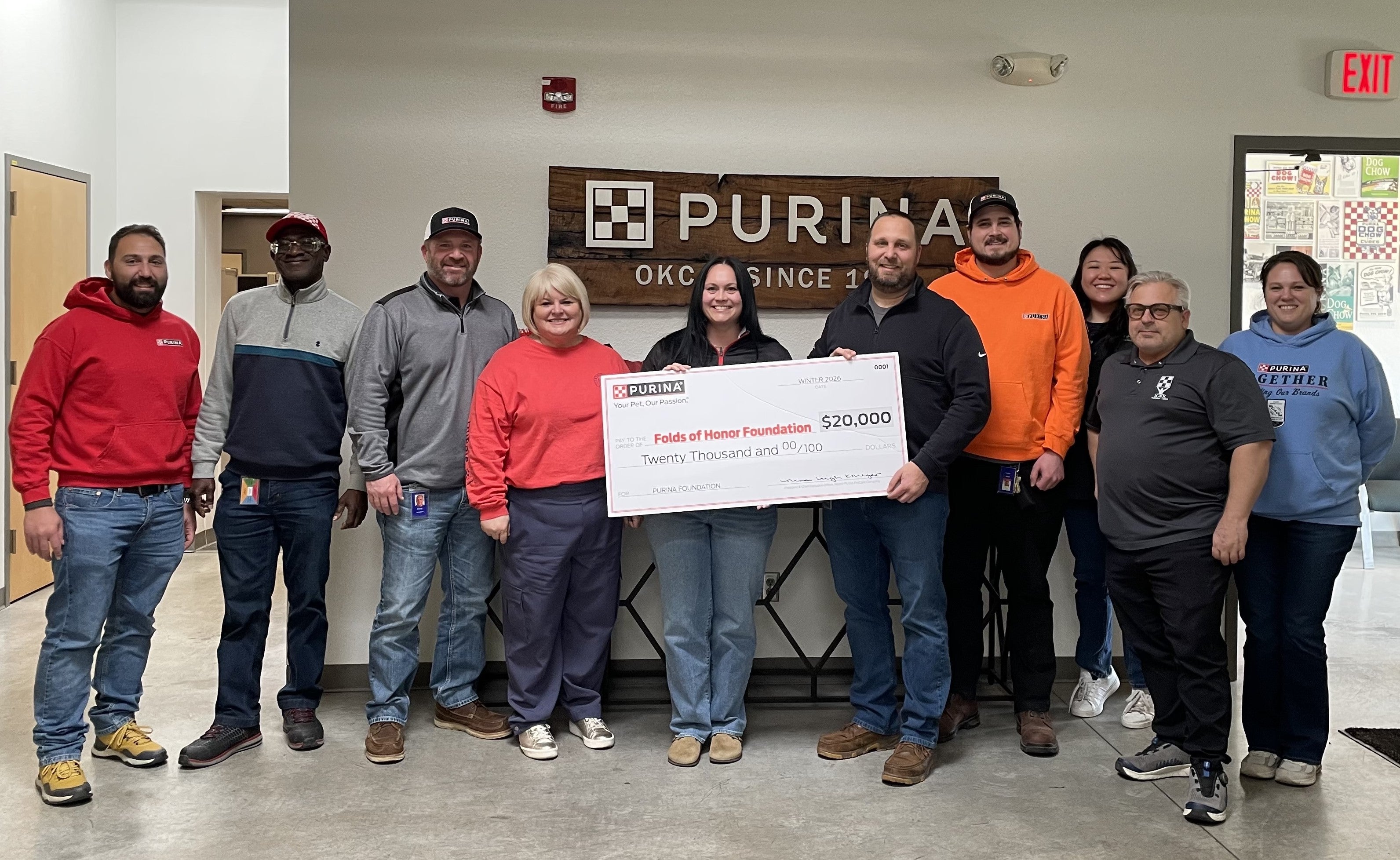 Group of people standing indoors holding a $20,000 Purina check for the Folds of Honor Foundation in front of a Purina OKC si