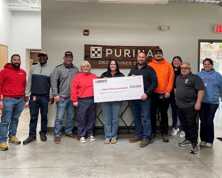 Group of people standing indoors holding a $20,000 Purina check for the Folds of Honor Foundation in front of a Purina OKC si