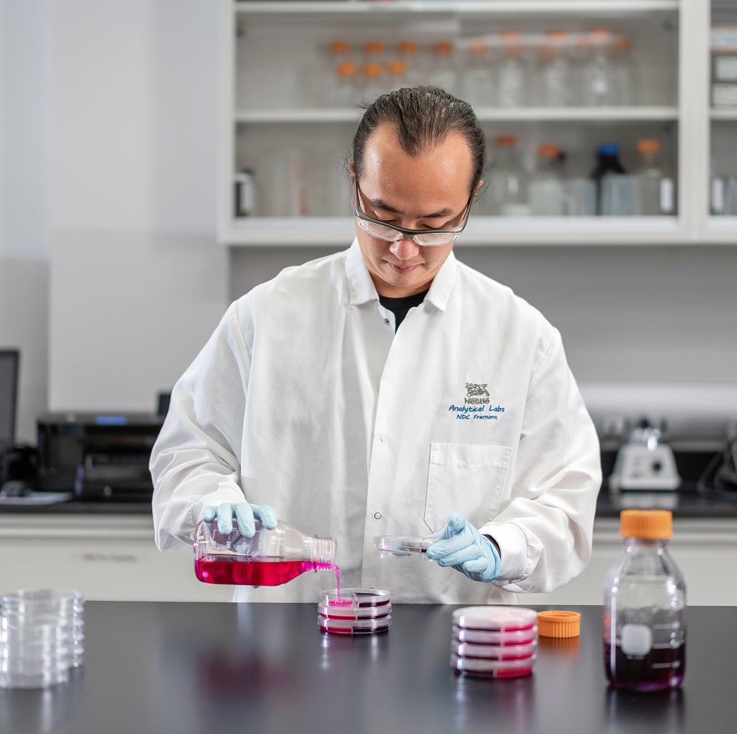 Scientist in a lab coat handling petri dishes with pink liquid in a laboratory.