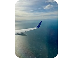 View of an airplane wing flying over a calm ocean under a partly cloudy sky.
