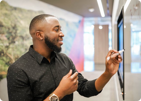 Man smiling while writing on a smart board in a modern office hallway.