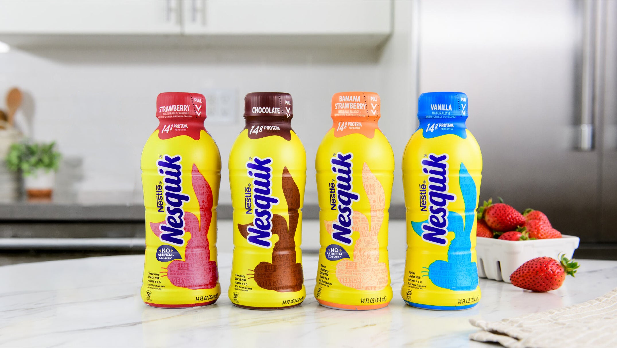 Four Nesquik bottles in different flavors on a kitchen counter with strawberries nearby.