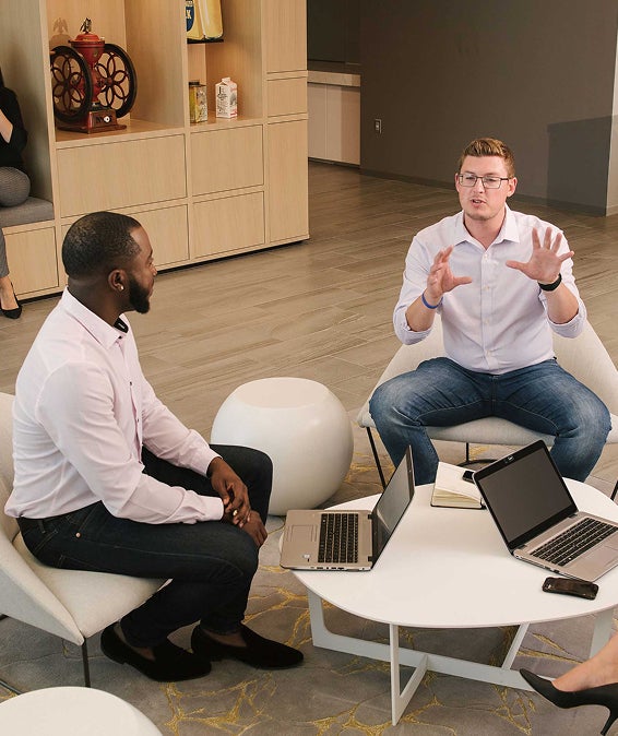 Two men in discussion at a modern office table with laptops and notebooks.