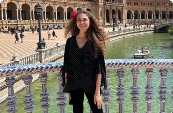 Woman with curly hair and a red flower standing by a colorful railing near a canal.