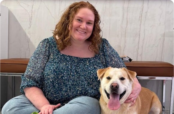 Smiling woman sitting on the floor with a happy dog indoors.