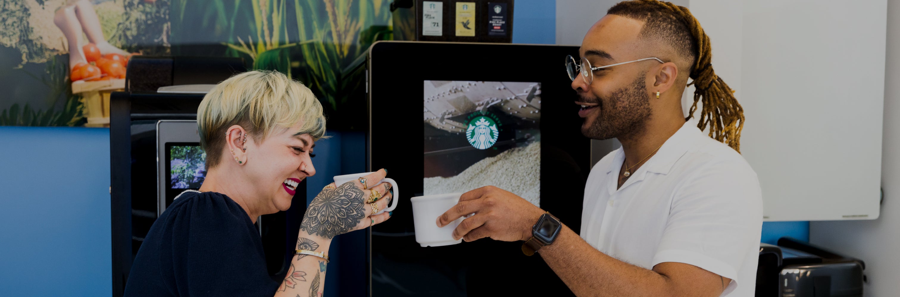 Two people smiling and clinking coffee mugs in front of a Starbucks coffee machine.