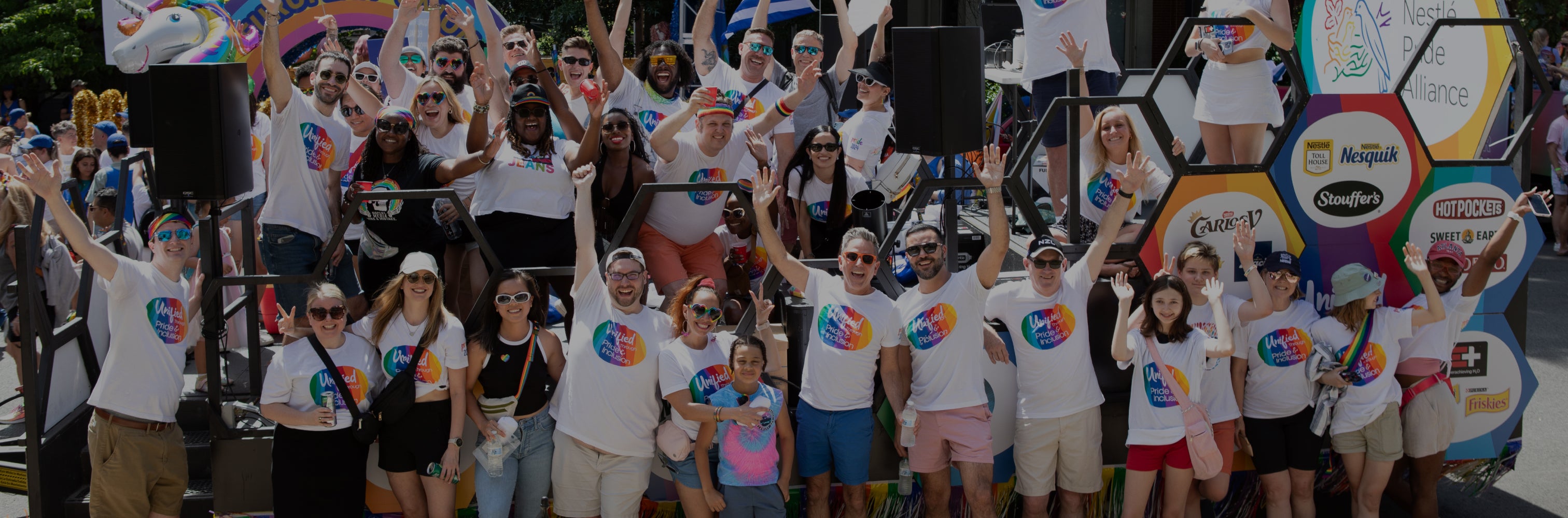Group of people in matching rainbow shirts celebrating at an outdoor event with colorful decor.