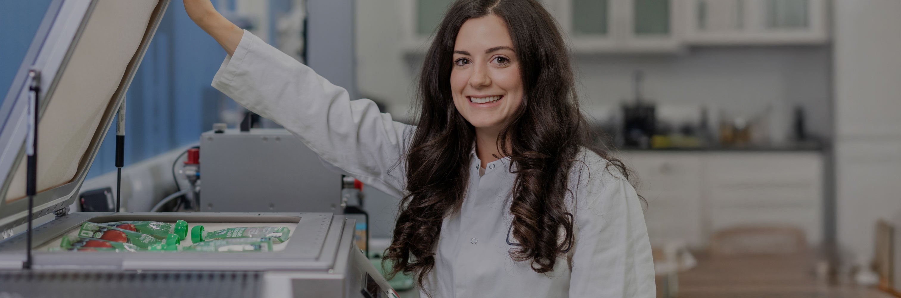 Smiling woman in lab coat standing by an open laboratory freezer.