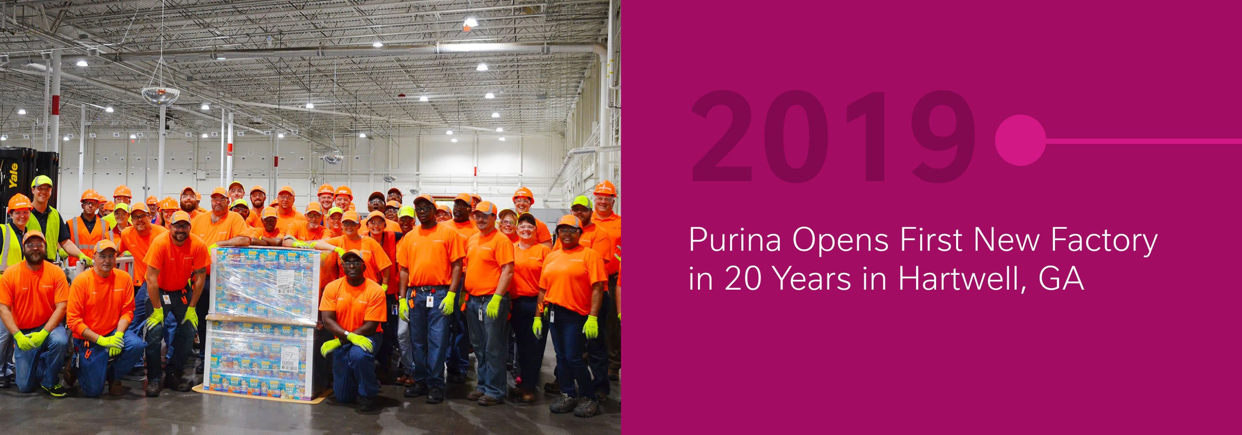 Group of workers in orange shirts posing in a factory, next to a timeline marking 2019.