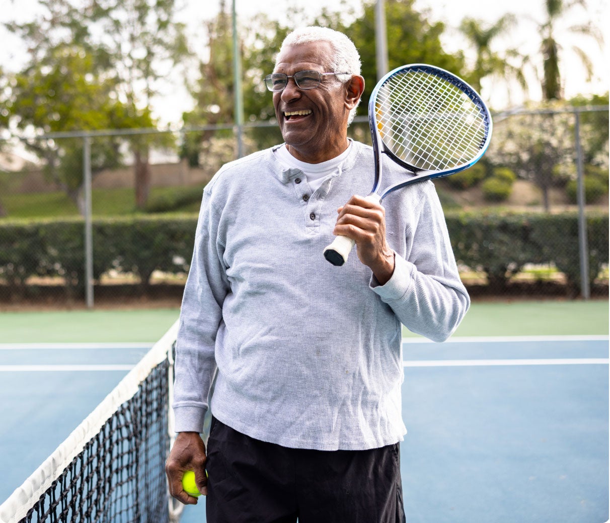 Smiling older man holding a tennis racket on an outdoor tennis court.