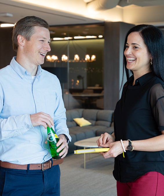Two colleagues smiling and talking in a modern office lounge area.