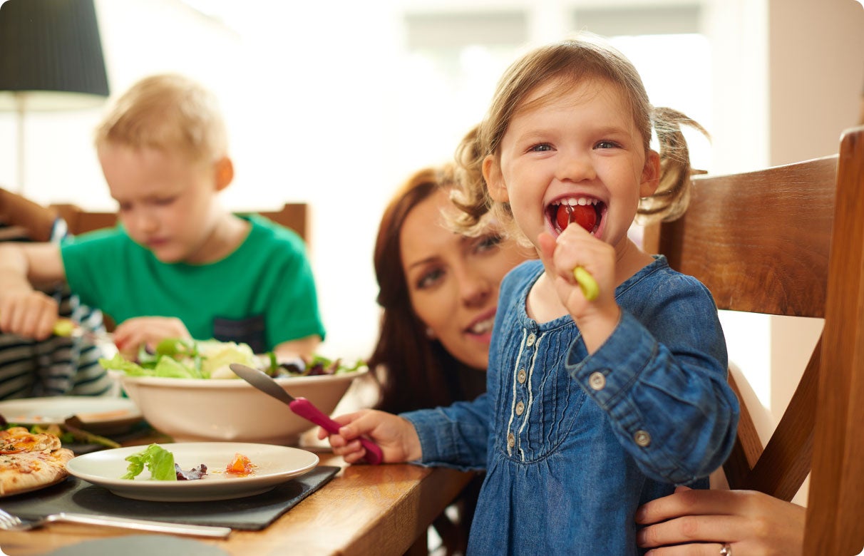 Smiling girl in blue dress eating at a table with family.
