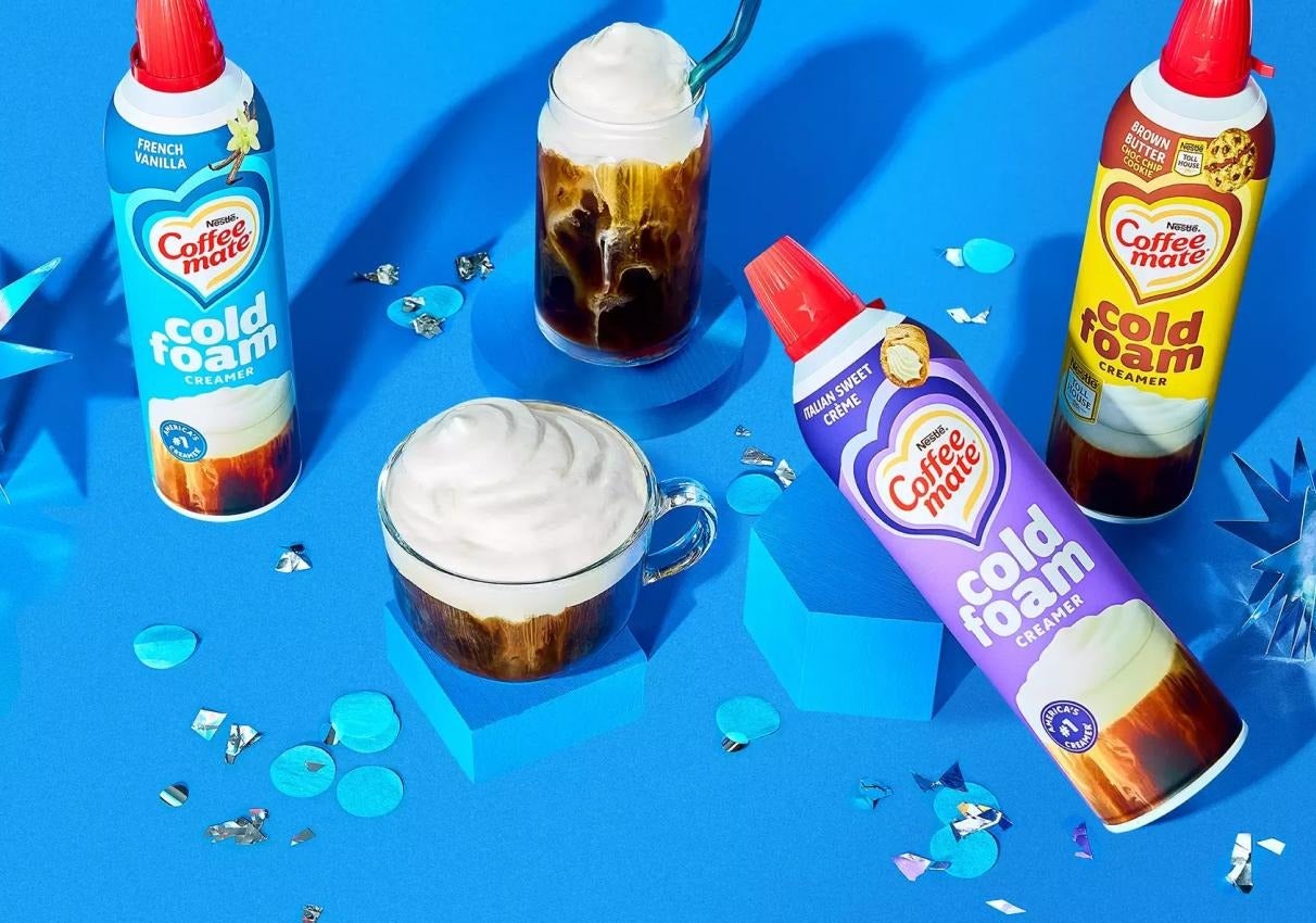 Coffee Mate Cold Foam Creamer cans with iced coffee topped with foam on a bright blue background.