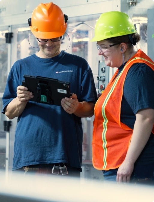 Two associates in hard hats reviewing a tablet on the plant floor