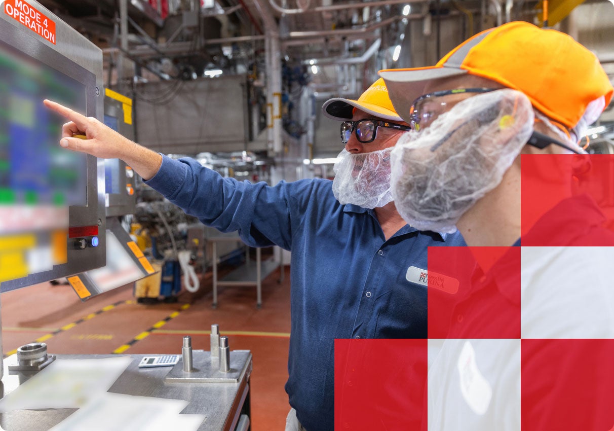 Two factory associates in hard hats reviewing a control screen