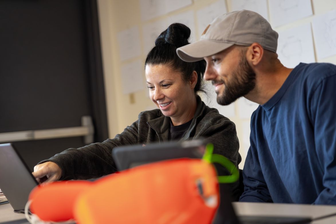 Woman and man sit together smiling near a computer screen in a factory setting