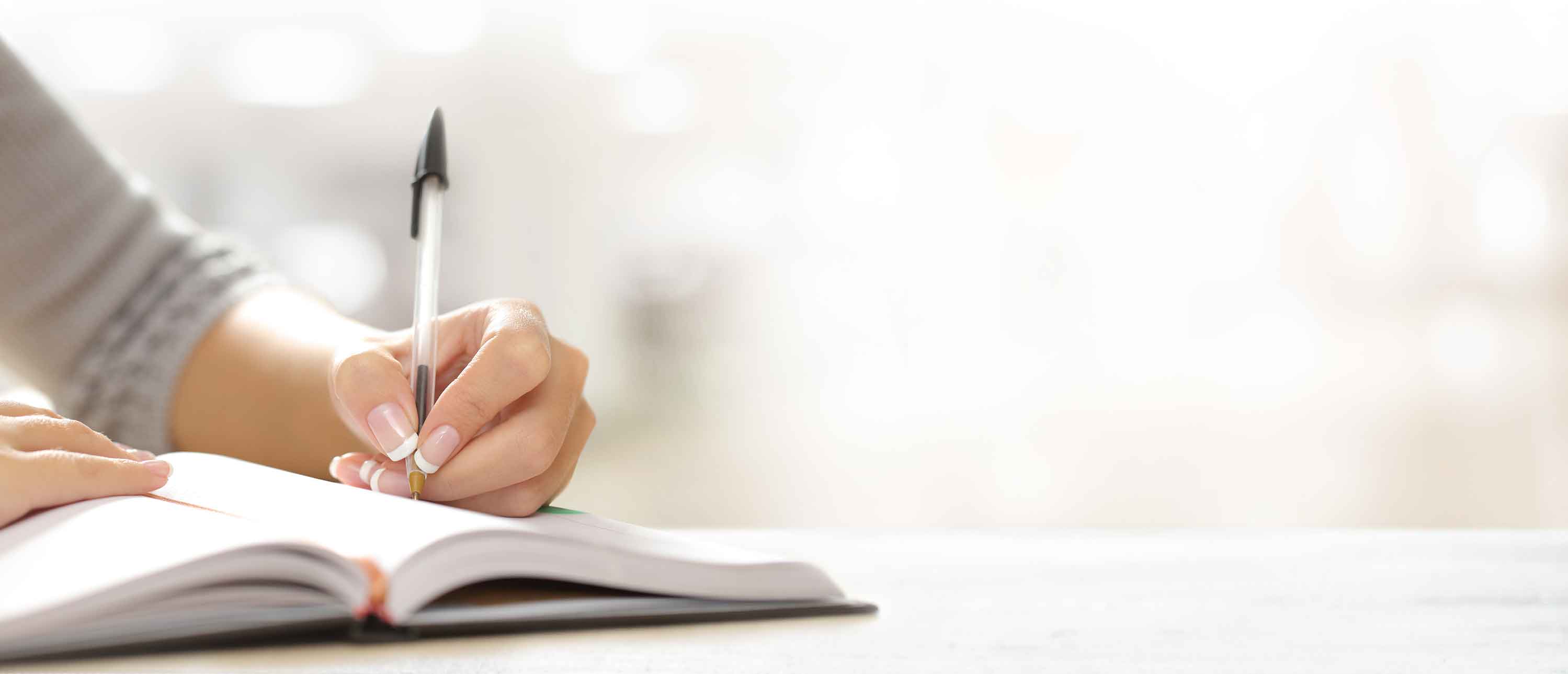 A hand holds a pen and writes something to a notebook