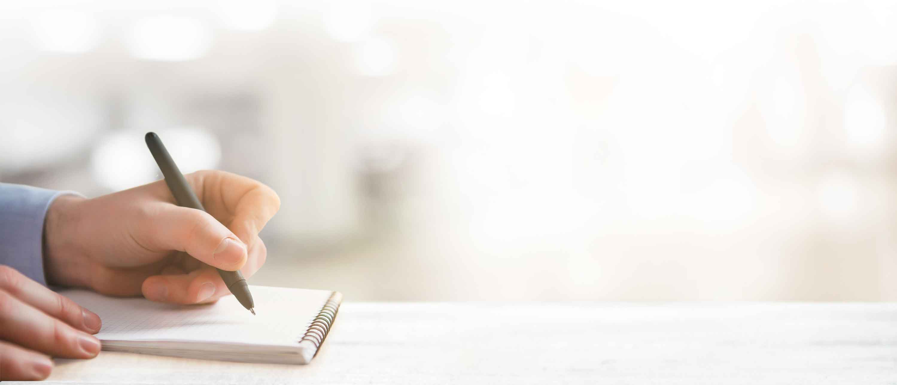 A hand holds a pen and writes something to a notebook