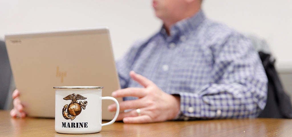 Man sitting at a desk with a laptop and a Marine mug