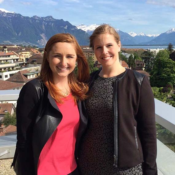 Two smiling women stand in the background of mountains