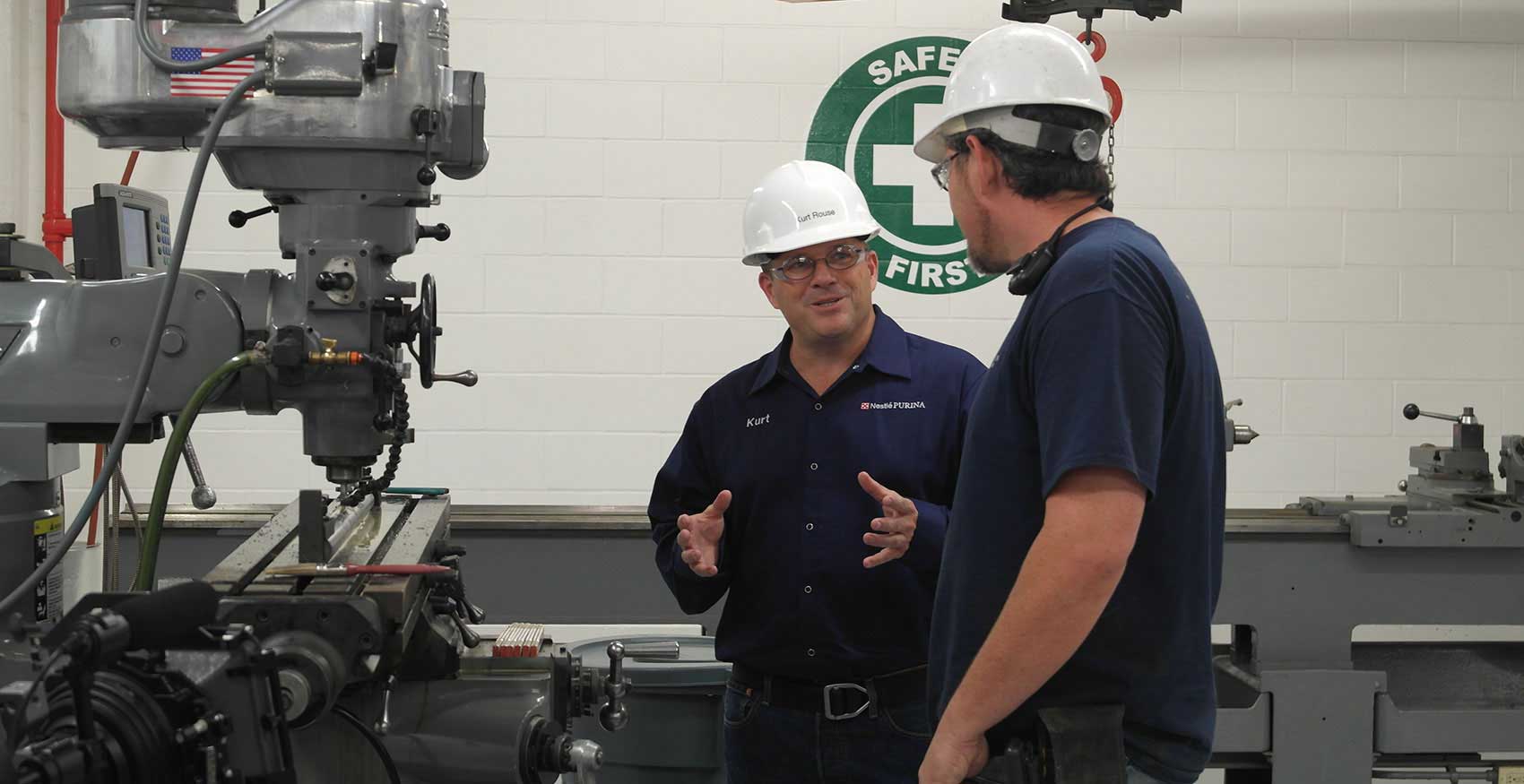 Two men talking on factory floor with hard hats on
