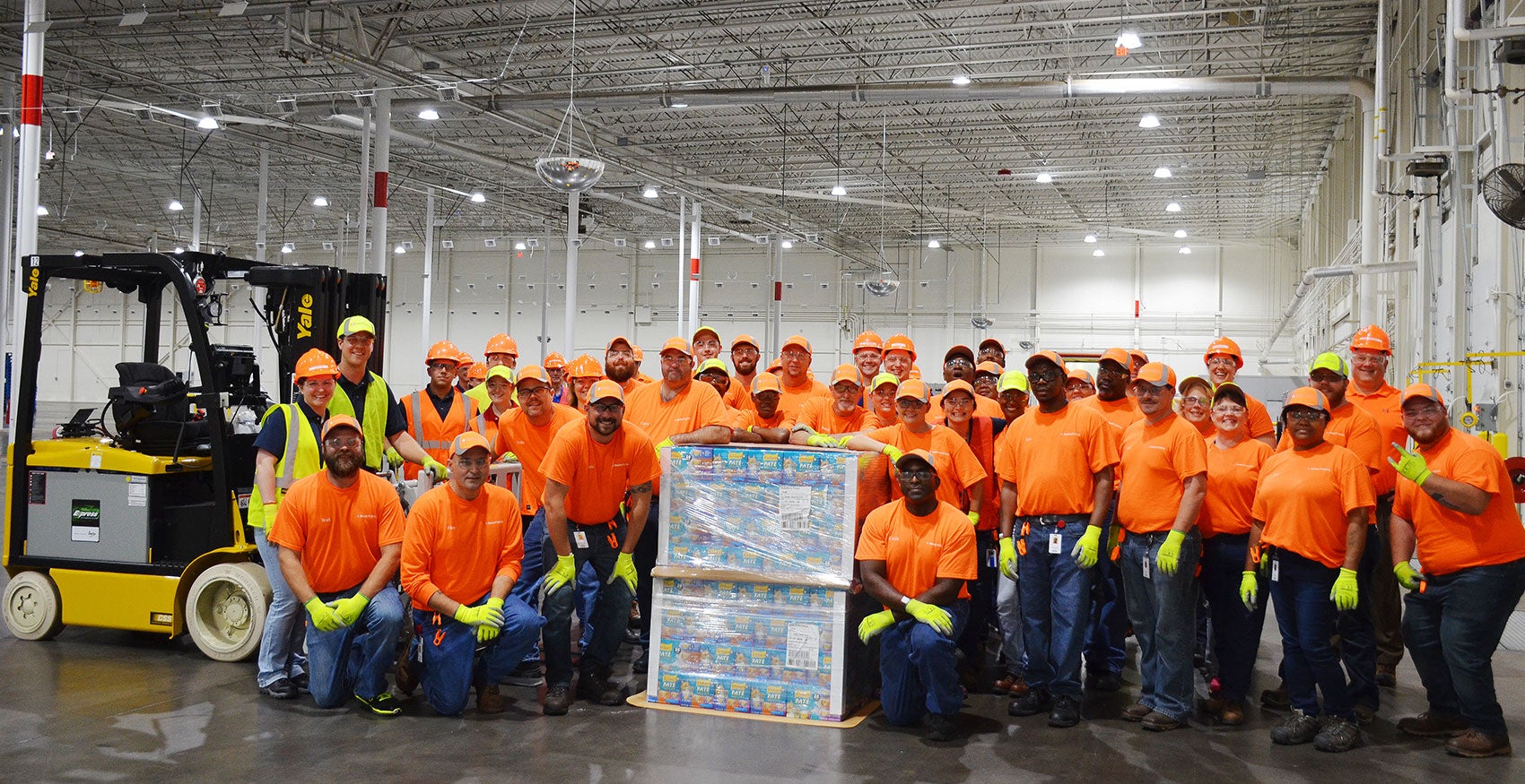 Team of factory workers gathered around for a group photo with packaging