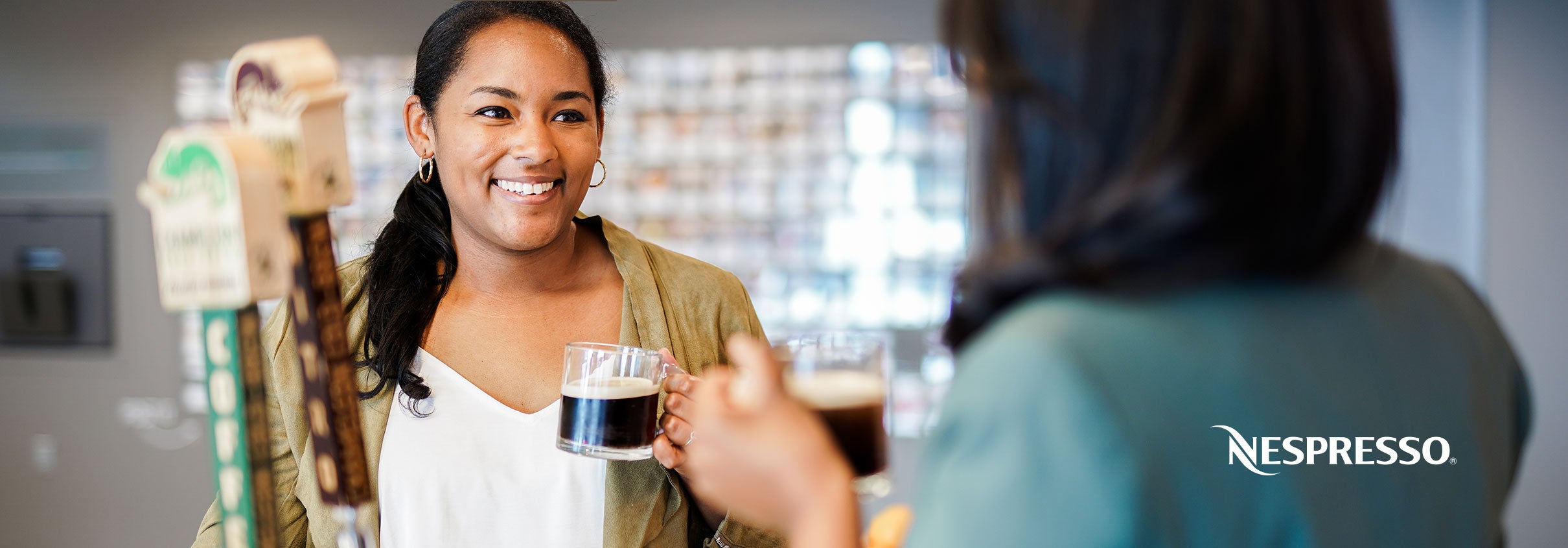 Two women smiling while drinking Nespresso in the office