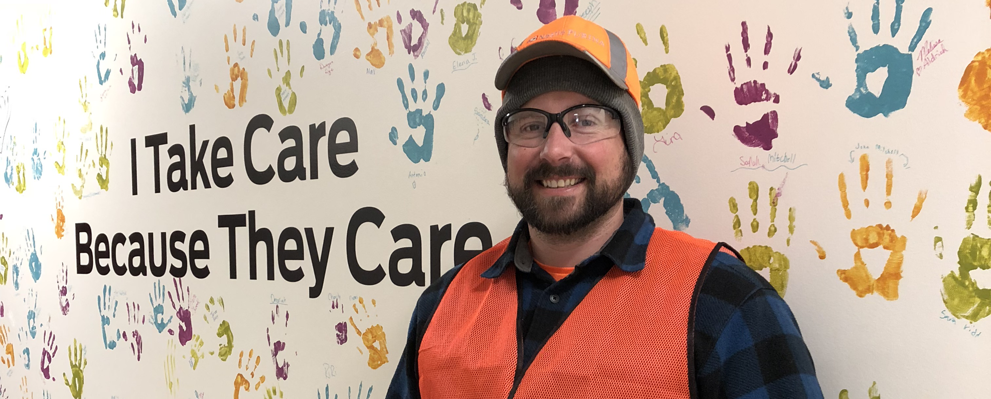 Man standing in front of wall of handprints which reads 'I Take Care Because They Care'