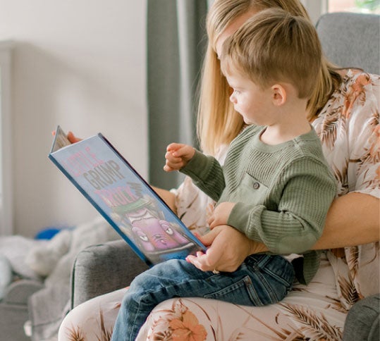 Toddler sitting on mom's lap reading a story in a rocking chair