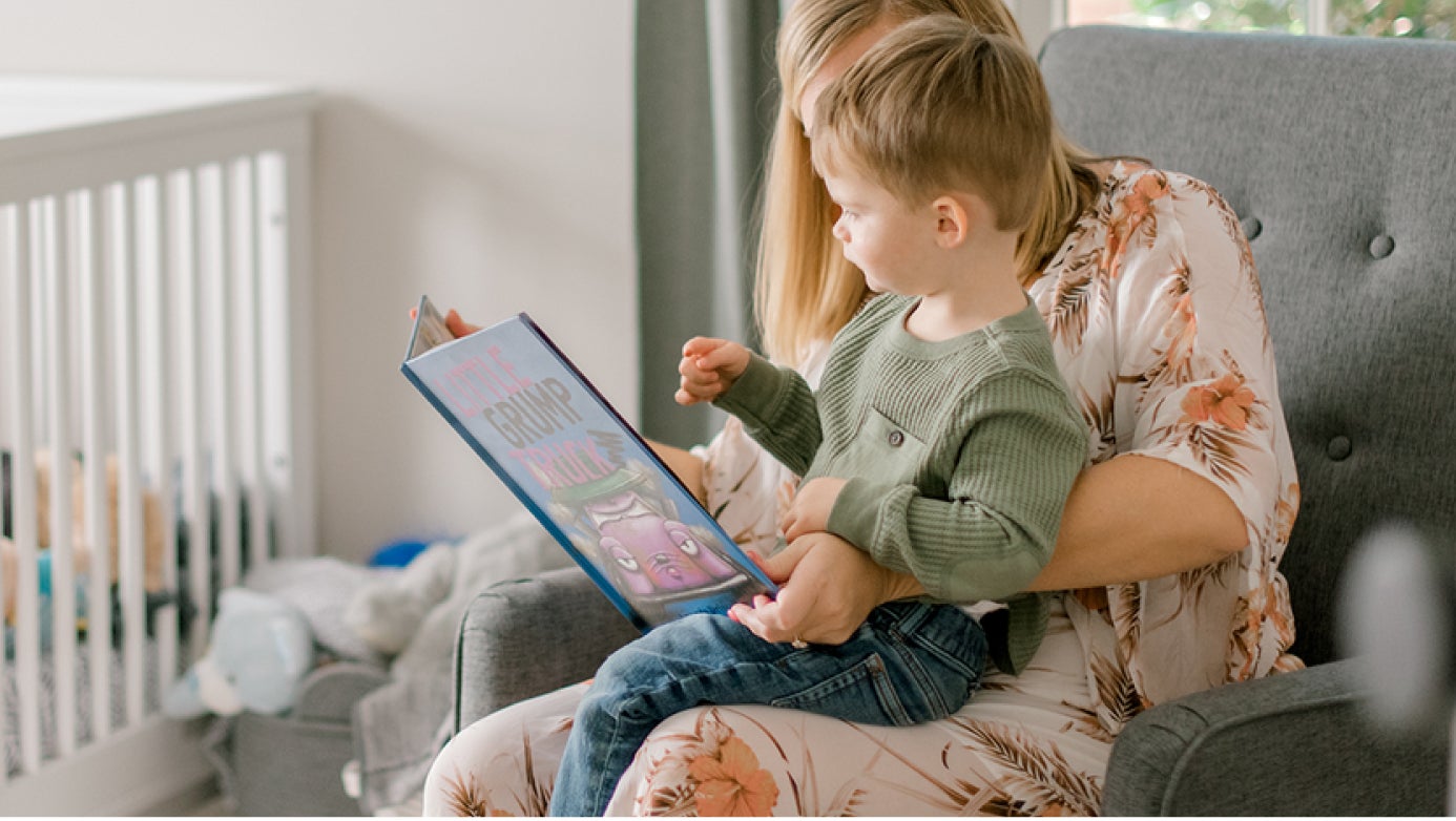 Toddler sitting on mom's lap reading a story in a rocking chair