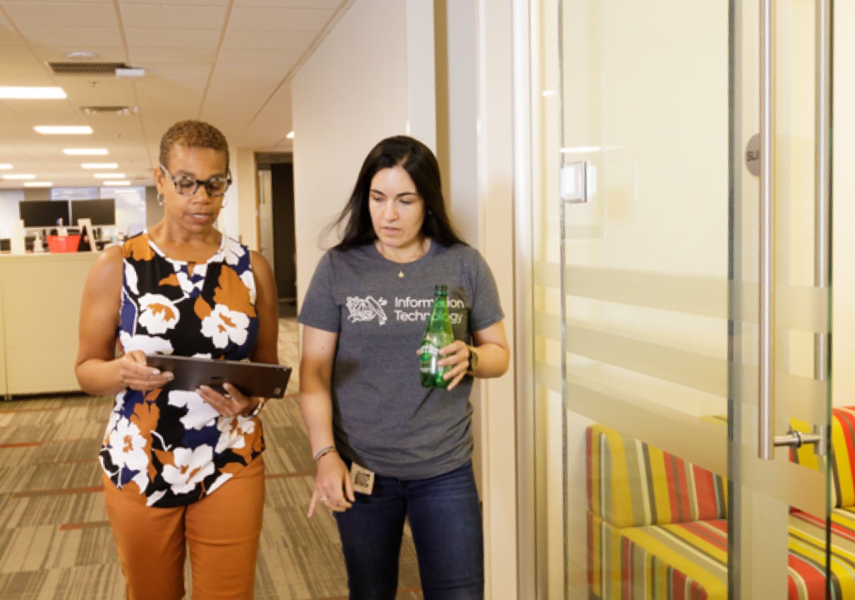 Two women walking through the office reviewing an ipad screen