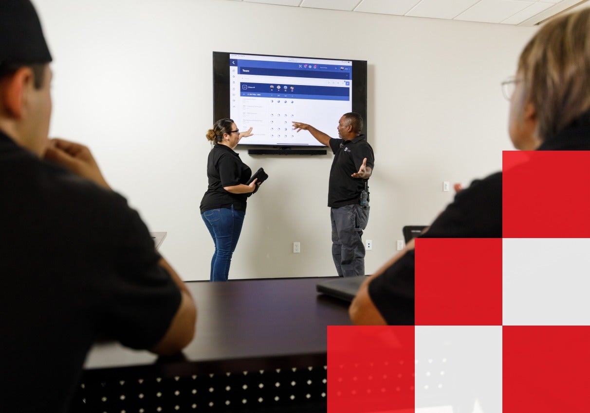 A diverse group of people gathered in a meeting room, focused on a large screen displaying important information.