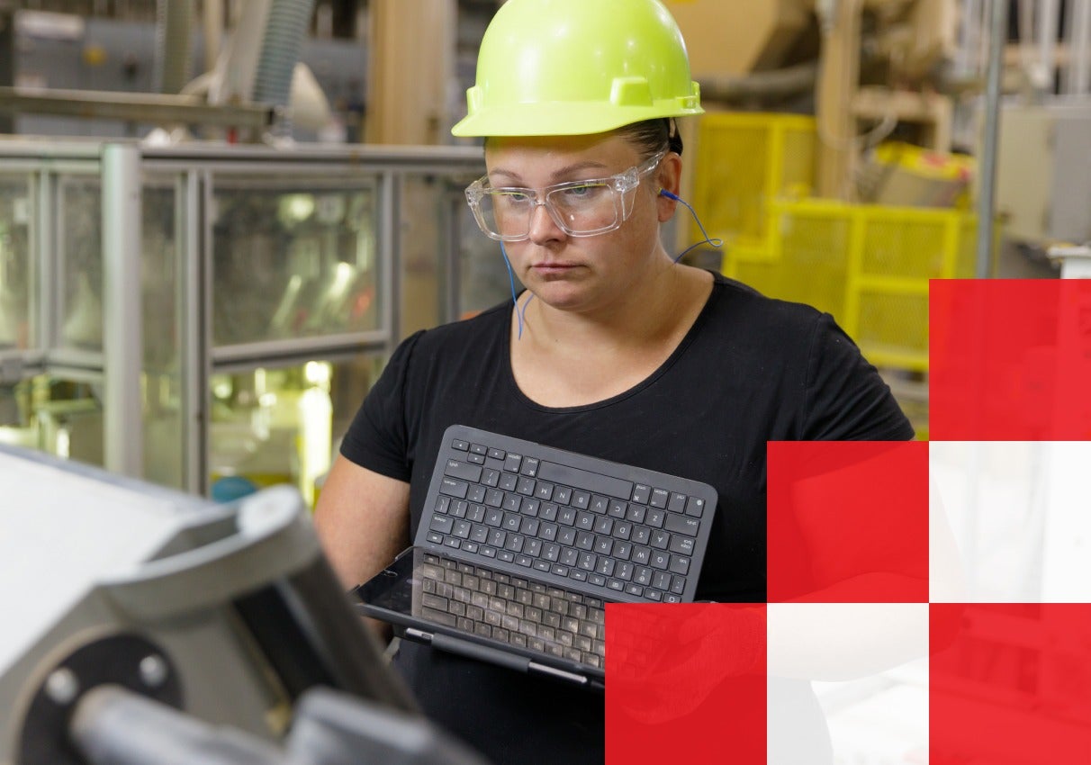 A woman wearing a hard hat and glasses, confidently holding a laptop in her hands, ready for work.