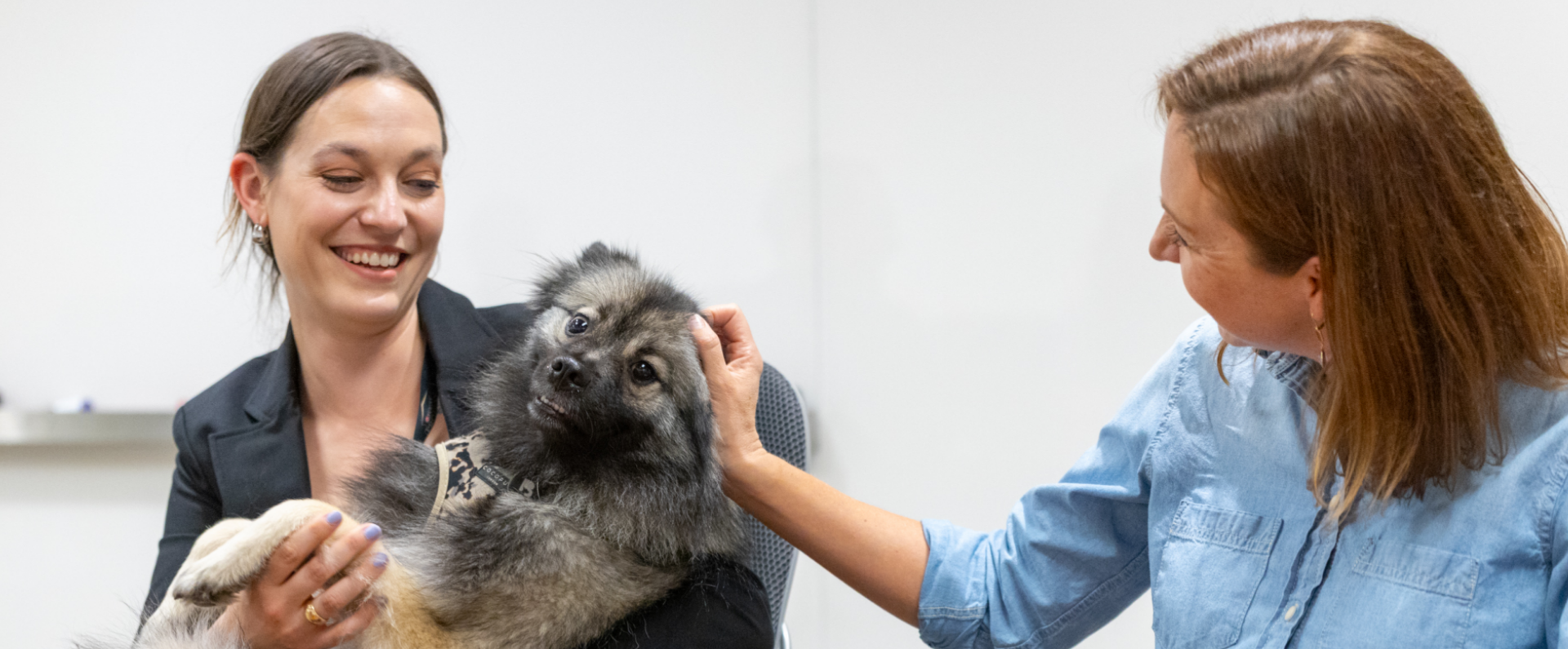 2 women smiling while holding and petting a dog