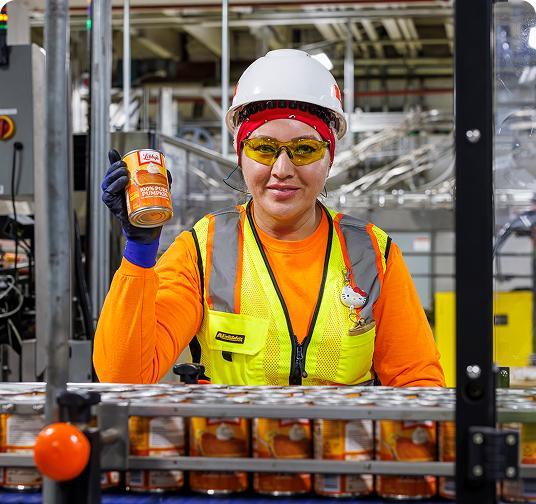 Worker in safety gear holding a can of pumpkin in a food processing factory.