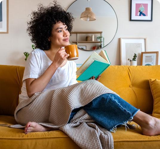 Woman sitting on couch reading book with coffee