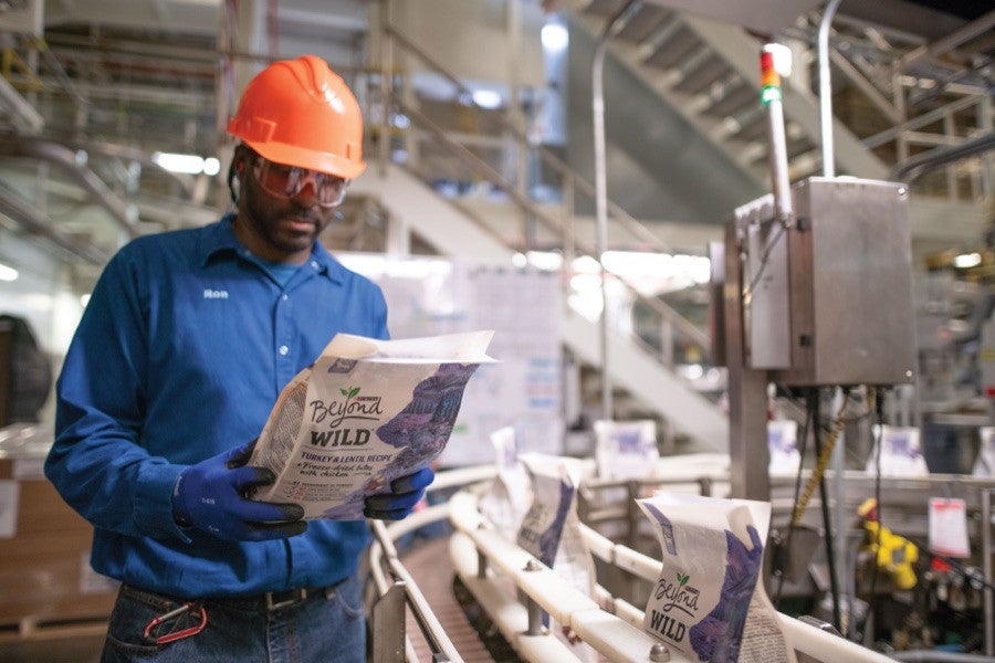 Factory associate in a hard hat inspecting a bag of Purina Beyond