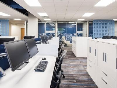 Open-plan office with white desks, blue dividers, and dual-monitor workstations