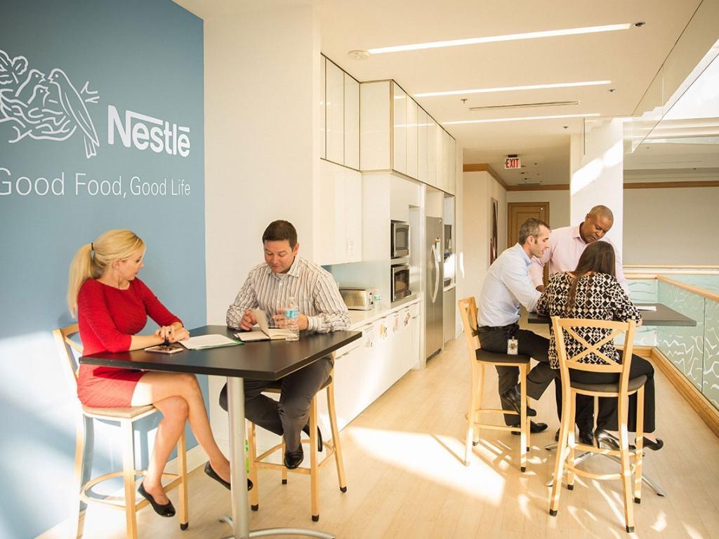 Collaborative Nestlé space with groups meeting at high tables near branded wall
