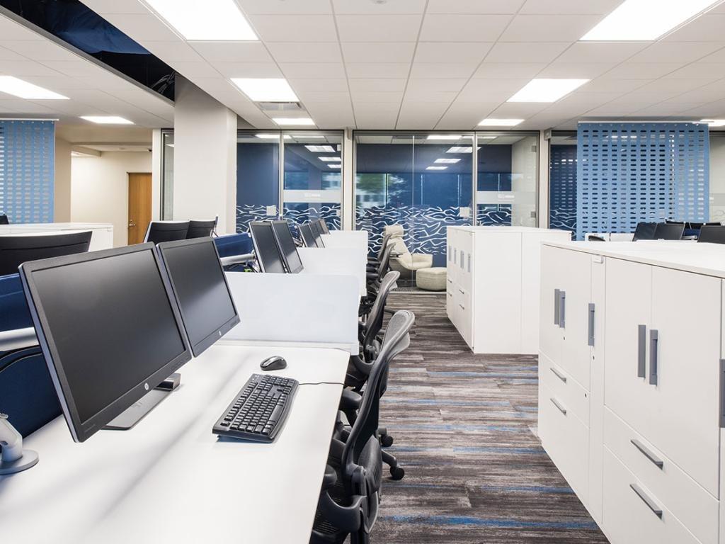 Open-plan office with white desks, blue dividers, and dual-monitor workstations