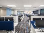 Open-plan office with white desks, blue dividers, and dual-monitor workstations
