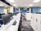 Open-plan office with white desks, blue dividers, and dual-monitor workstations