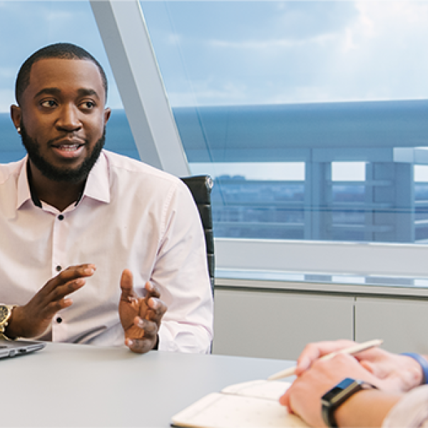 Employee sitting at a desk with his laptop talking with a colleague