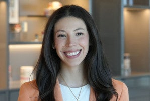 Woman with long dark hair smiling in a modern office setting.