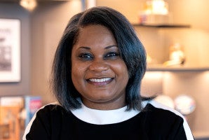 Woman with shoulder-length hair smiling in a warmly lit indoor setting.