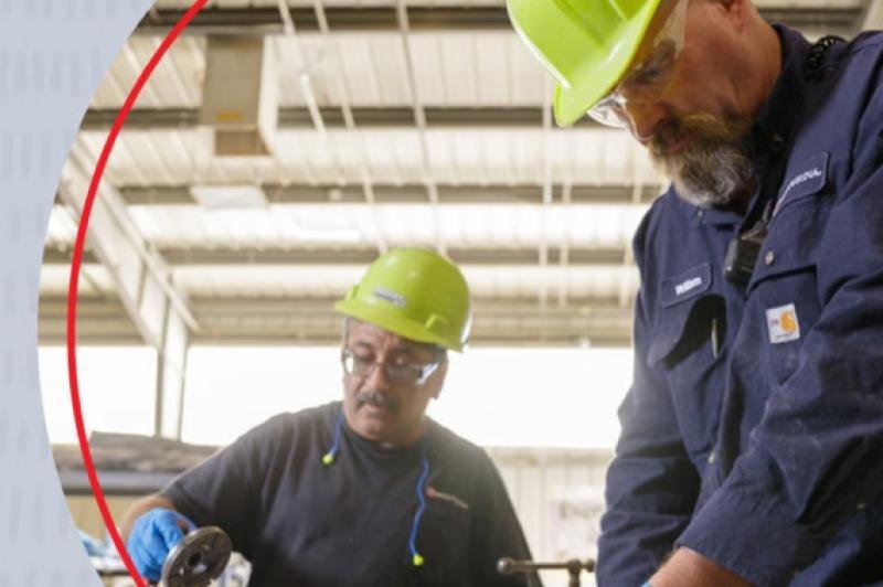 Two men in hard hats diligently operating a machine, showcasing teamwork and focus in a work environment
