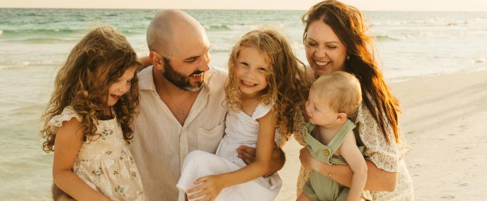 Smiling family of five on a sunny beach, laughing together near the shoreline.